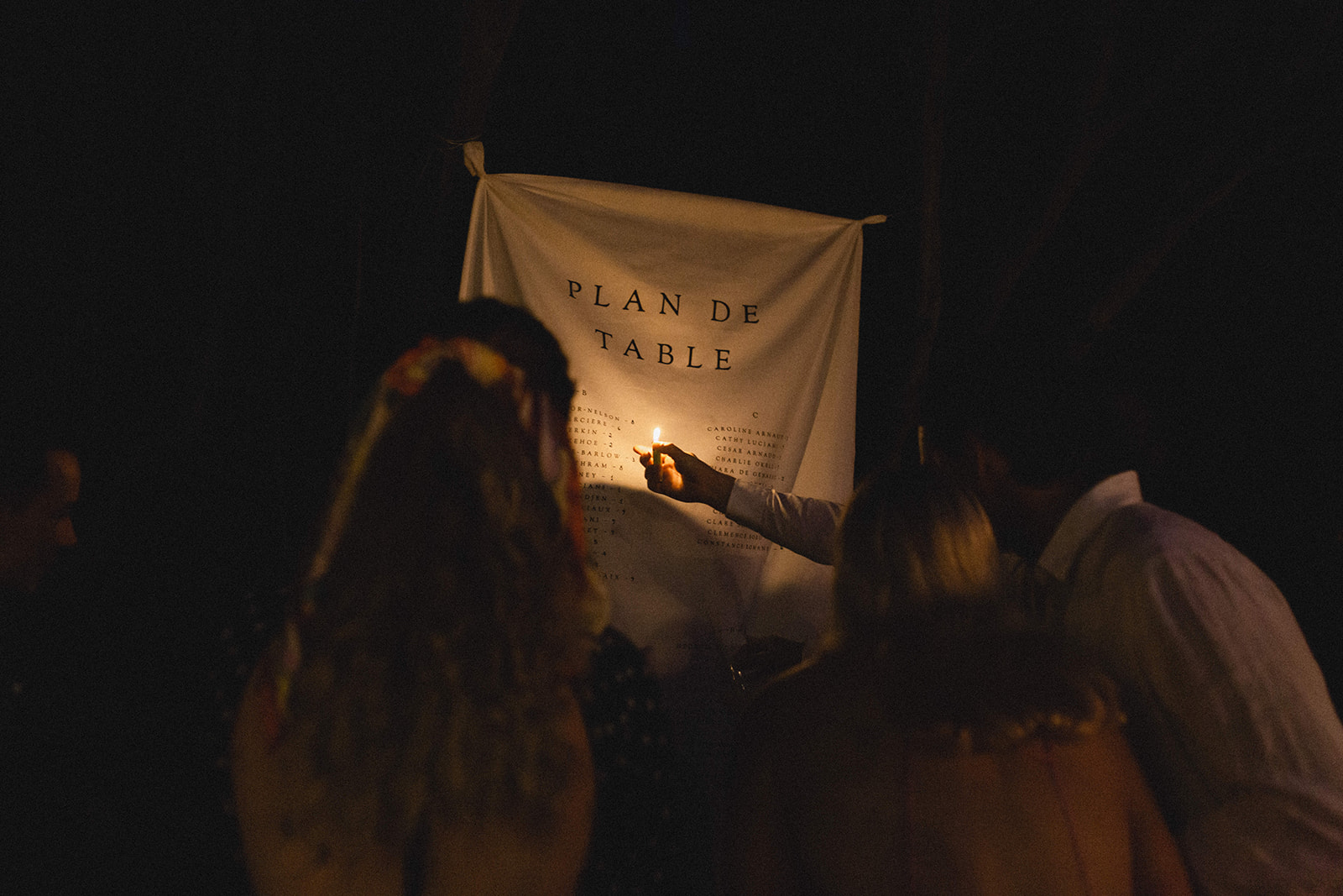 Guests in the night looking at the plan de table with a lighter light during a humanist wedding in Corsica